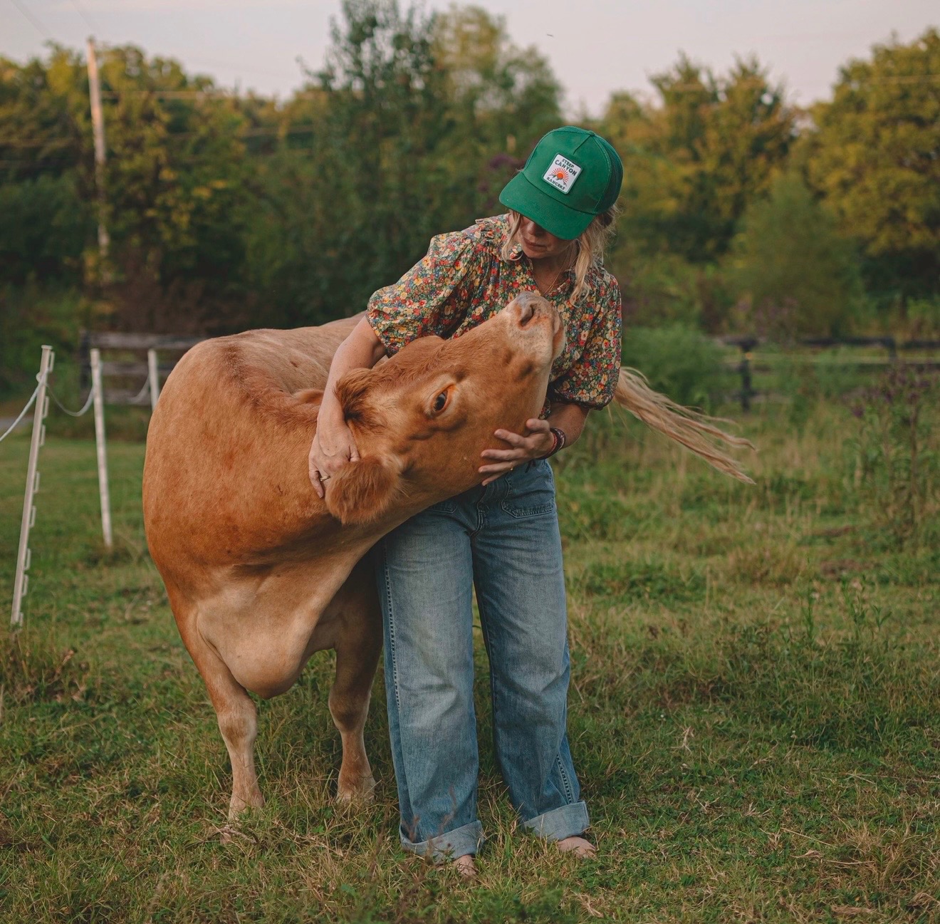 Sarah cuddling a brown cow in a grassy field at Fremont Farm